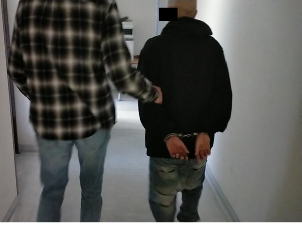 Policjant eskortujący skutego podejrzanego korytarzem.