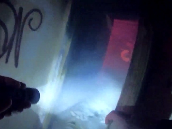 Zbliżenie latarki oświetlającej pokryte graffiti ściany ciemnego, prawdopodobnie opuszczonego budynku.