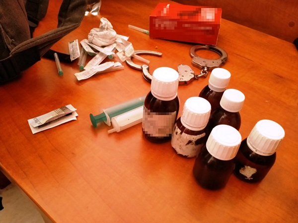 Przybory do narkotyków, w tym strzykawki, tabletki i butelki, skonfiskowane podczas obławy narkotykowej na Pradze. Widoczne są również kajdanki.