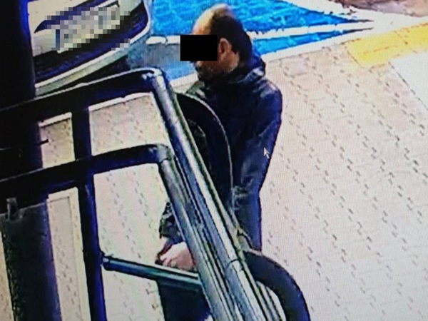 Obraz z monitoringu przedstawiający mężczyznę w ciemnej kurtce stojącego obok pojazdu.