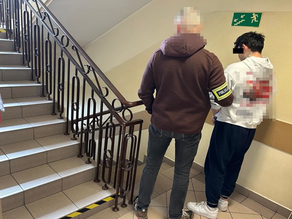 Policjant eskortujący podejrzanego po schodach.
