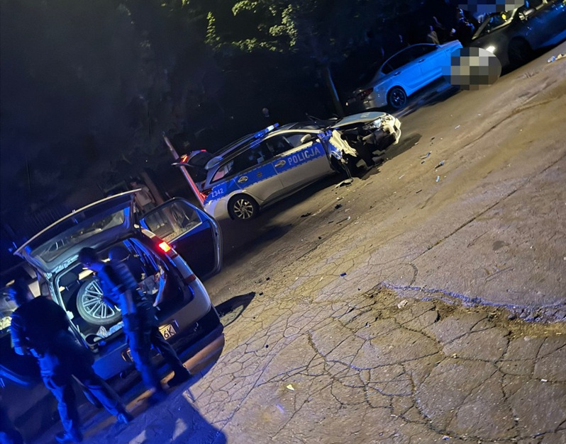 Uszkodzony radiowóz i inne pojazdy na miejscu wypadku nocnego. W pościgu zderzył się z radiowozem