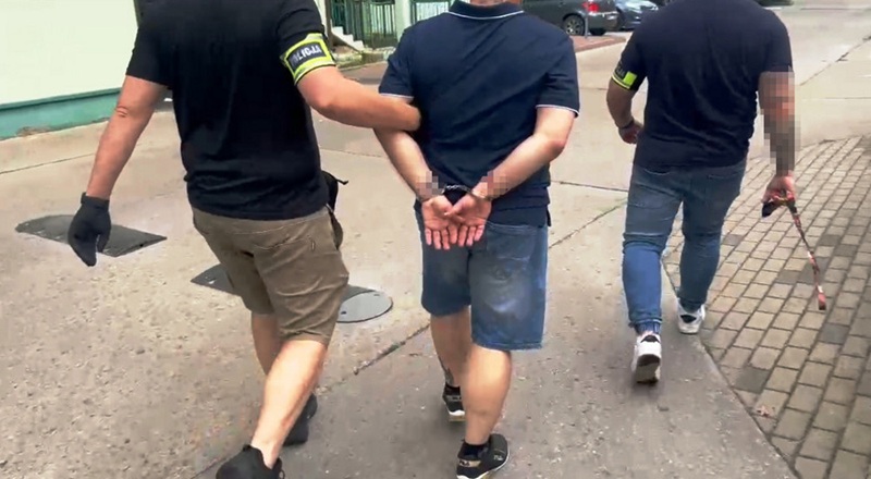 Policjanci eskortujący podejrzanego w kajdankach. 69 ofiar perfumowego oszustwa fot. policja, mat. pras.