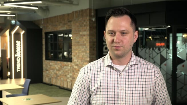 Mężczyzna w kraciastej koszuli rozmawia, tło biura Trend House