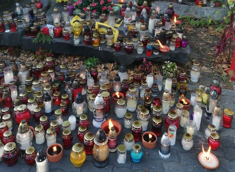 Liczne zapalone świece i lampy wotywne w miejscu pamięci.
