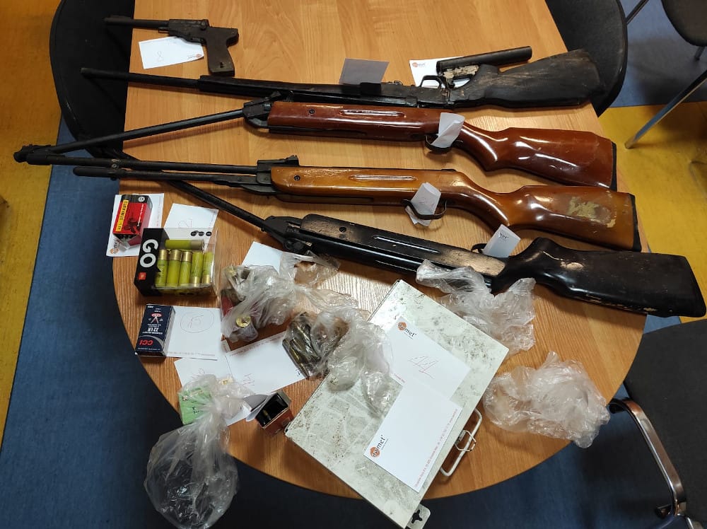 Zarekwirowano broń palną i amunicję: cztery karabiny i pistolet z różnymi nabojami wyłożone na stole.