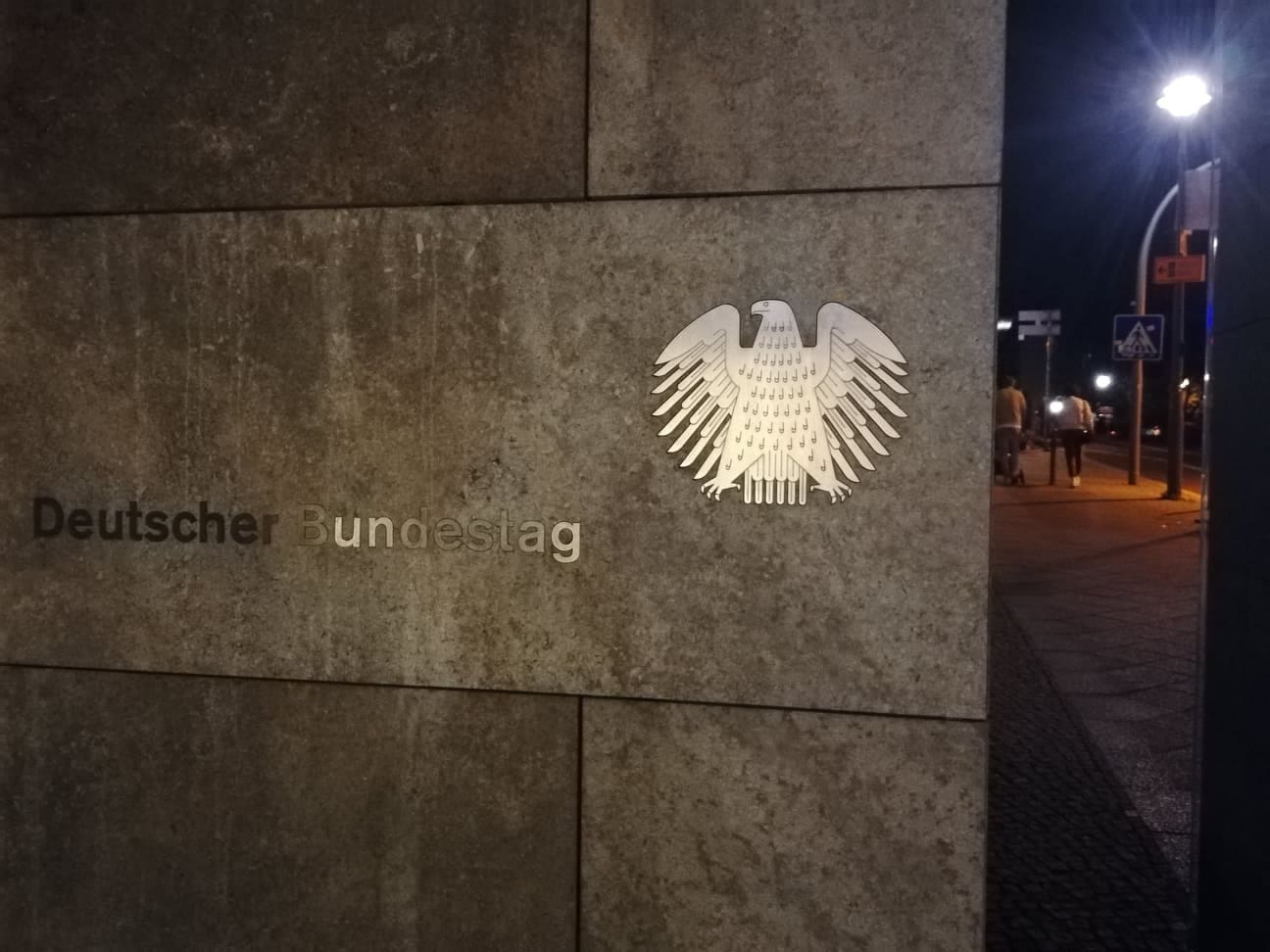 Budynek niemieckiego Bundestagu nocą, na zdjęciu widoczny jest orzeł federalny i nazwa budynku.
