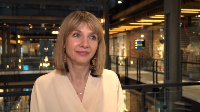 Kobieta z blond włosami sięgającymi do ramion, ubrana w beżowy top