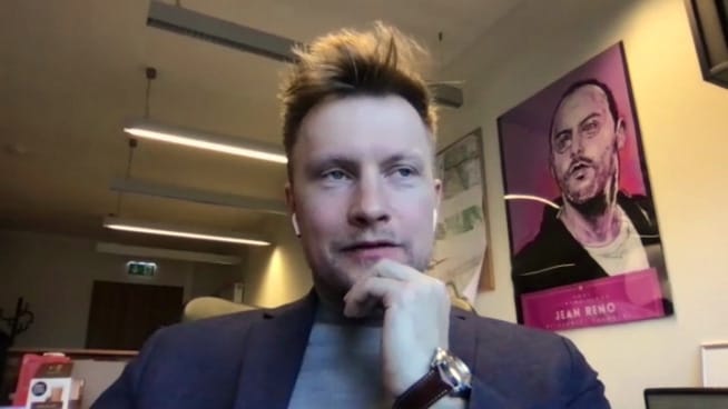 Mężczyzna w garniturze, zamyślony wyraz twarzy, plakat Jean Reno w tle