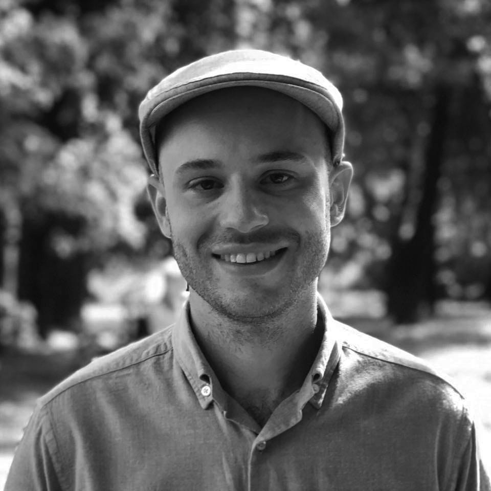 Zdjęcie mężczyzny w czapce gazeciarza, uśmiechającego się na zewnątrz.