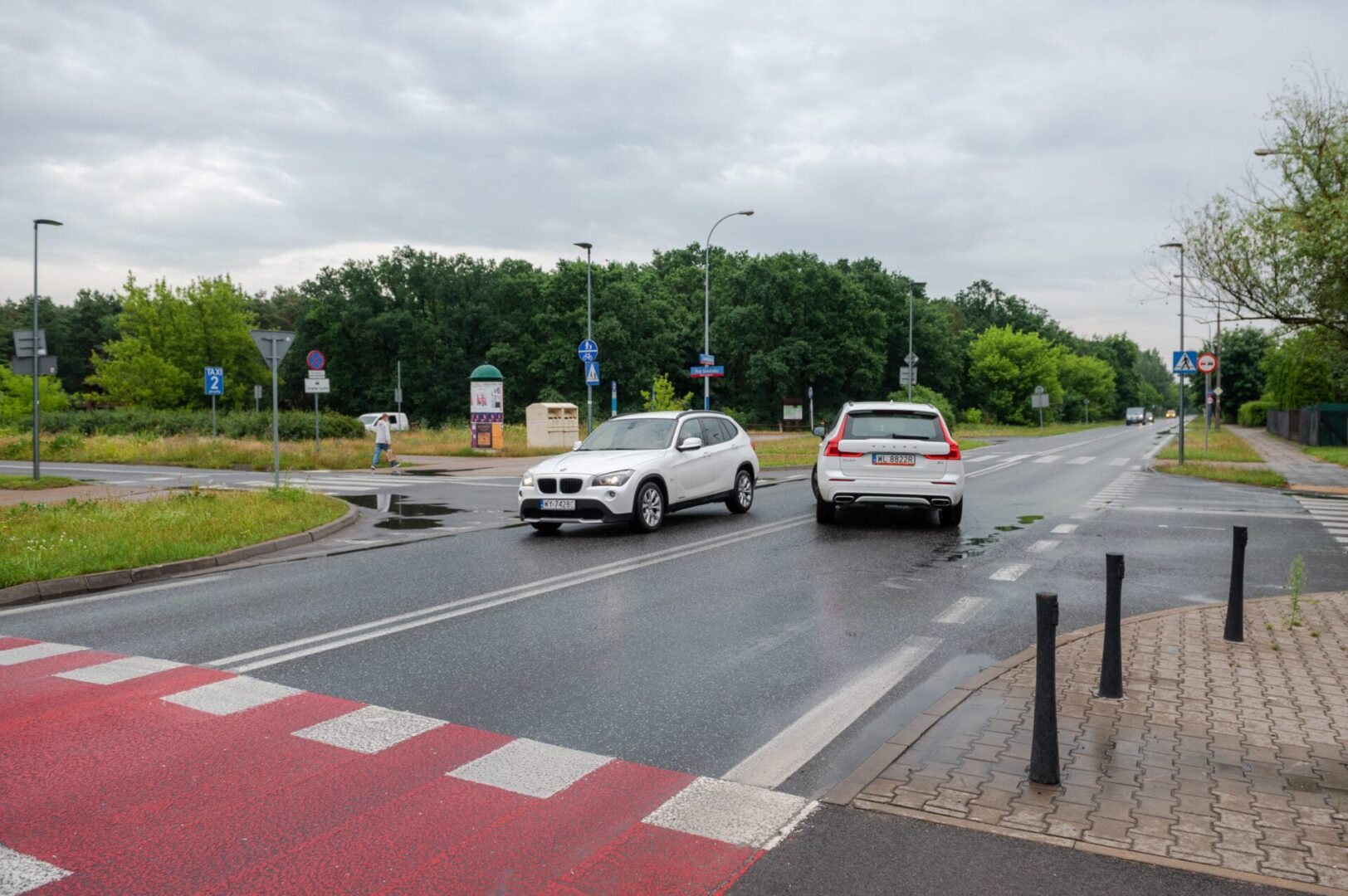 Dwa białe SUV-y na przejściu dla pieszych w deszczowy dzień.