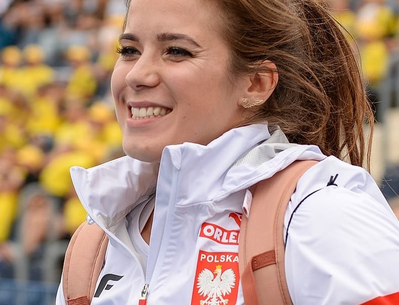 Uśmiechnięty polski sportowiec w białej kurtce z godłem narodowym