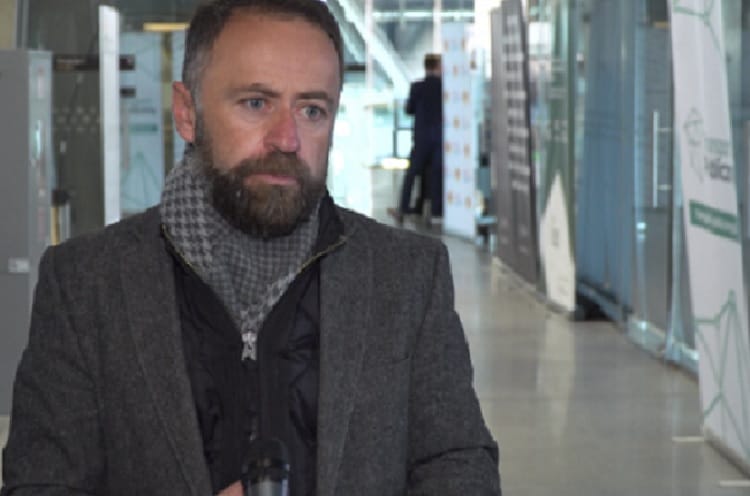 Mężczyzna z brodą ubrany w szary płaszcz i szalik