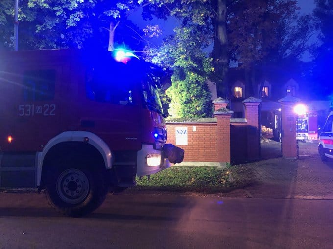 Wóz strażacki w nocy przed ceglanym budynkiem. Reagowanie kryzysowe.