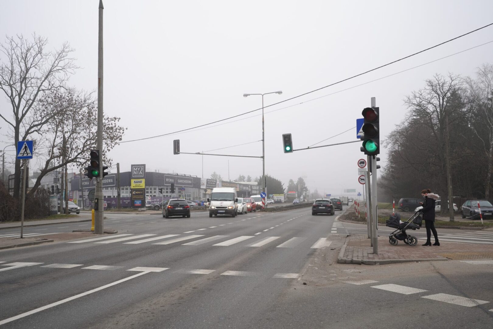 Piesi przechodzący przez ulicę na skrzyżowaniu ze światłami w mglisty dzień.