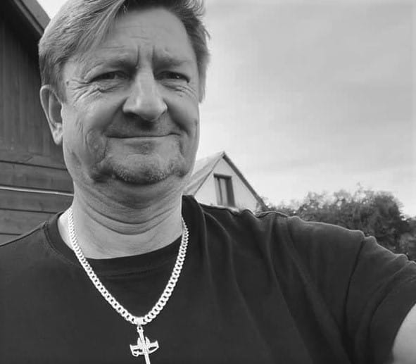 Mężczyzna w średnim wieku ze srebrnym łańcuszkiem i naszyjnikiem z krzyżem.