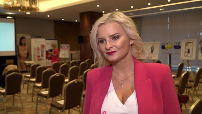 Kobieta w różowym żakiecie na konferencji, przemawiająca na podium