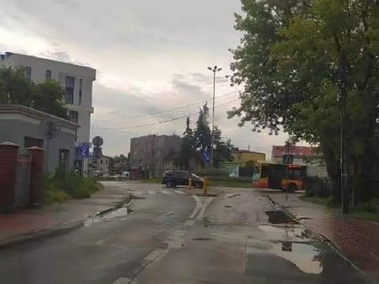 Deszczowy widok na ulicę z budynkami, samochodami i autobusem.