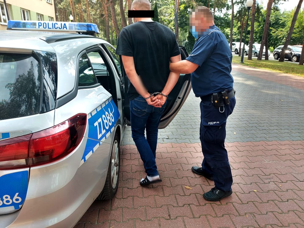 Policjant aresztujący podejrzanego w kajdankach w pobliżu radiowozu. POLICJA