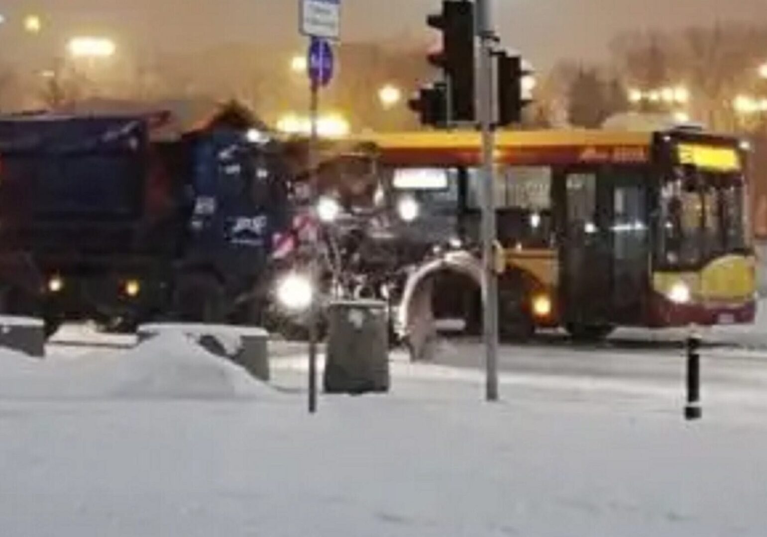 Scena z pokrytą śniegiem ulicą, autobusem, ciężarówką i pługiem śnieżnym.