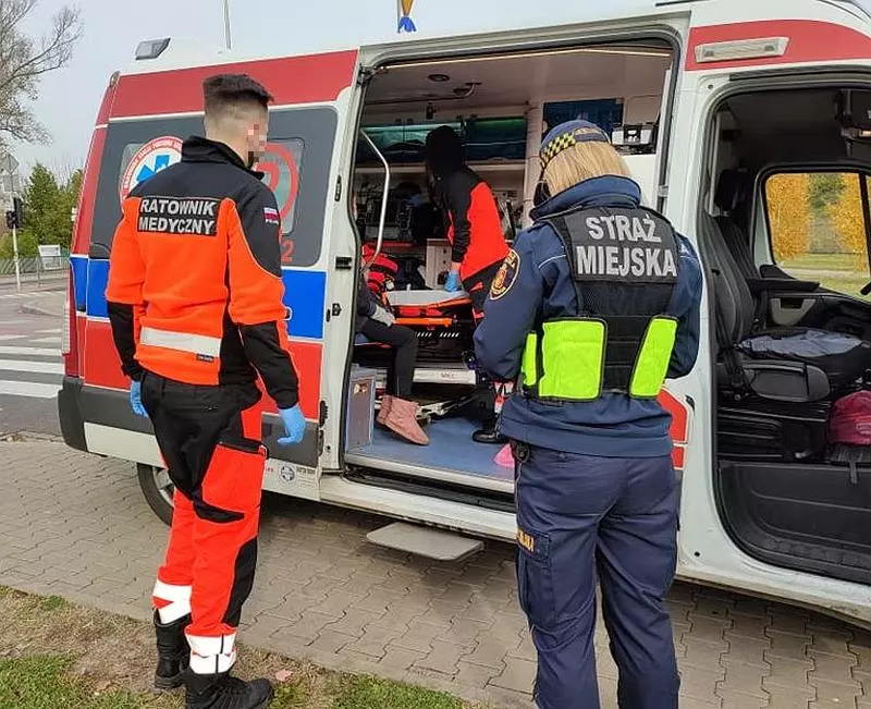 Ratownicy medyczni pomagają pacjentowi w karetce. Na mundurze widoczny napis „Straż Miejska”.
