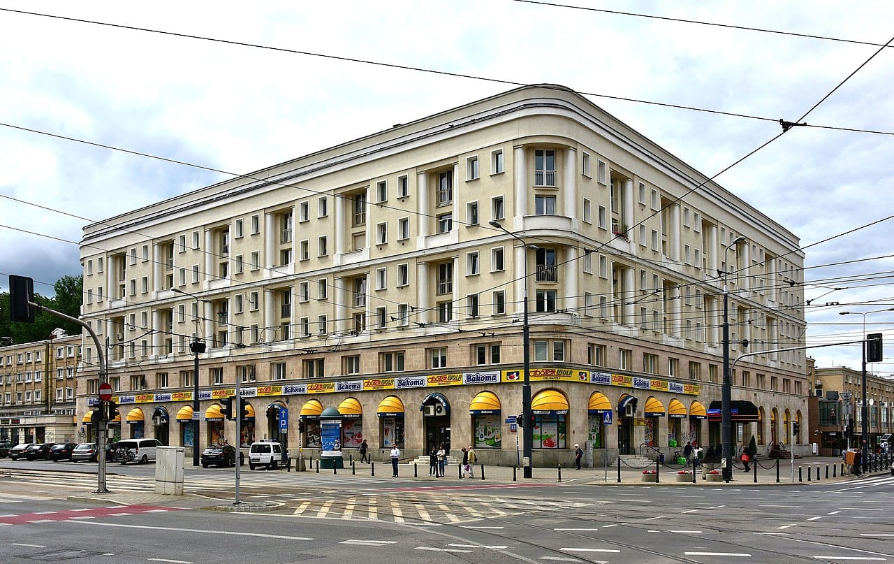 Duży beżowy budynek w stylu art déco z żółtymi markizami i szyldem „Bakomia”.