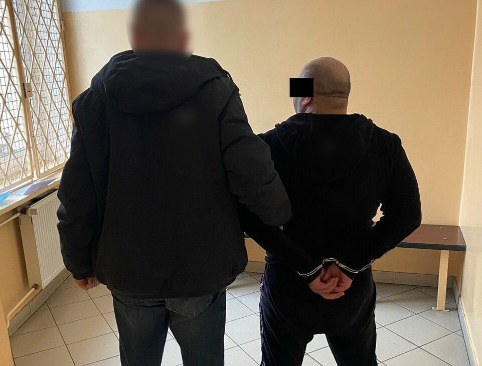 Dwóch mężczyzn w kajdankach, widok z tyłu, twarz jednego mężczyzny jest niewyraźna