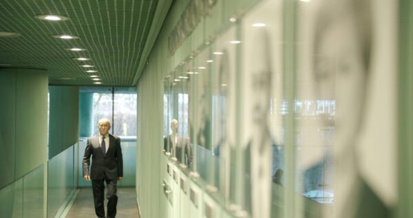 Biznesmen idący korytarzem z oprawionymi portretami.