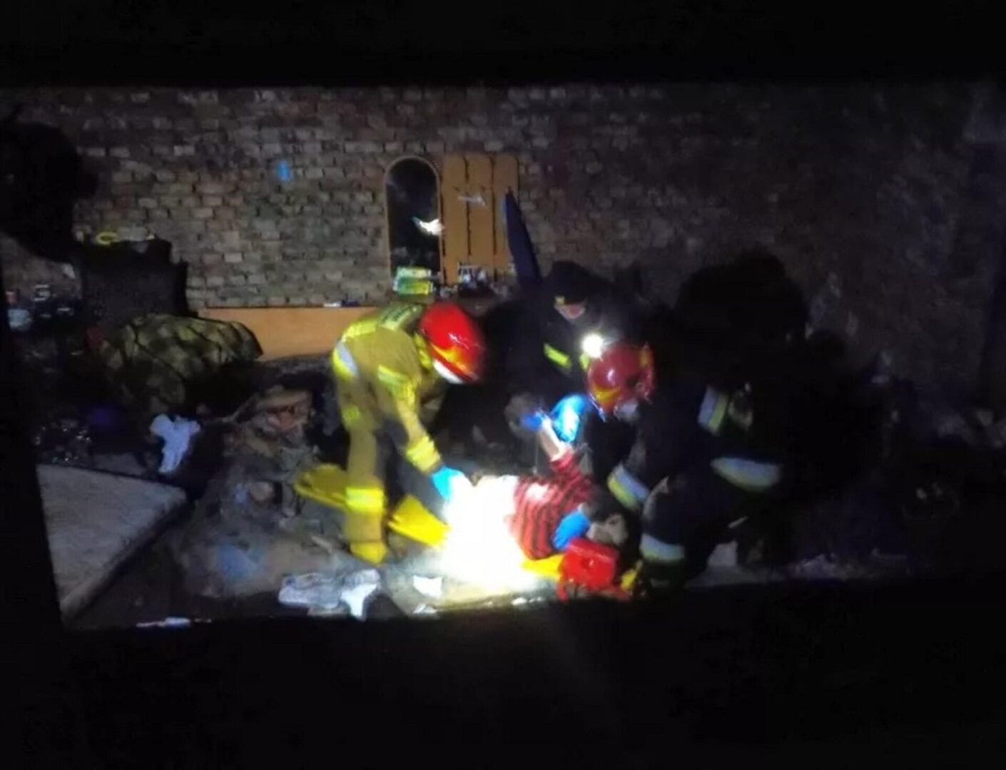 Ratownicy medyczni udzielają pomocy medycznej osobie na noszach w ciemnym, uszkodzonym pomieszczeniu.