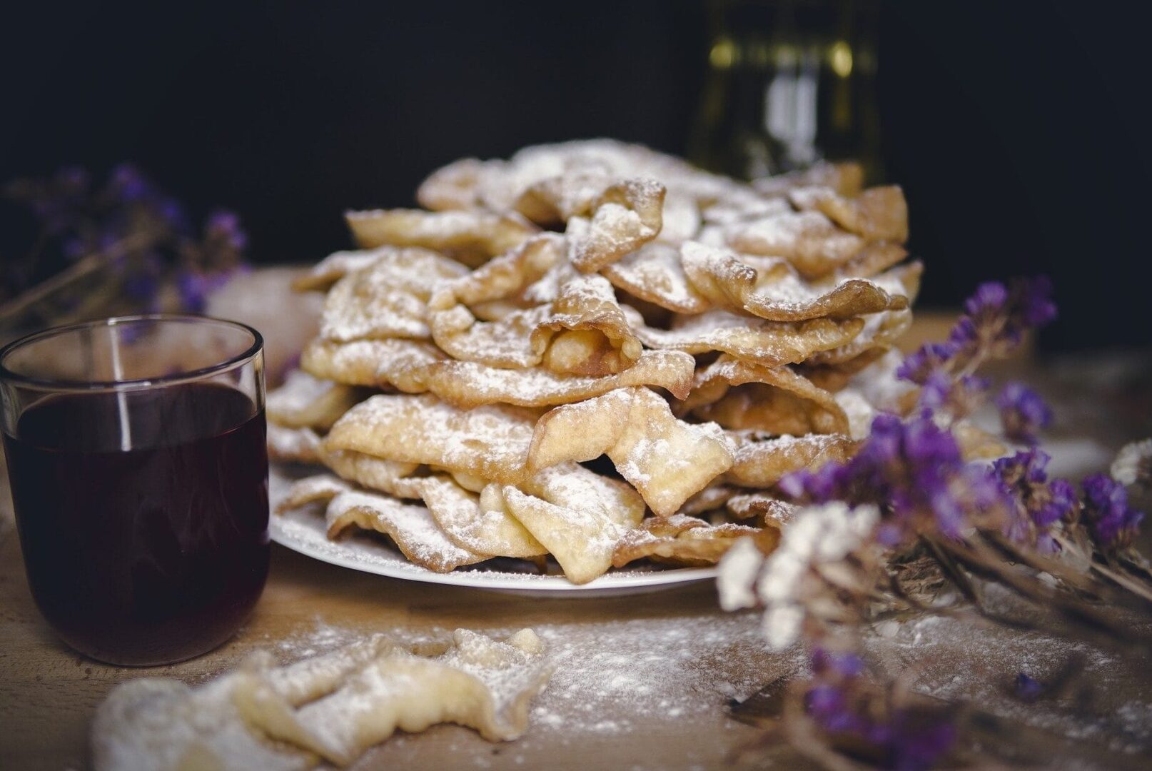 Chrupiące, posypane cukrem pudrem ciasteczka w kształcie skrzydełek fasolki na talerzu z lampką czerwonego wina.