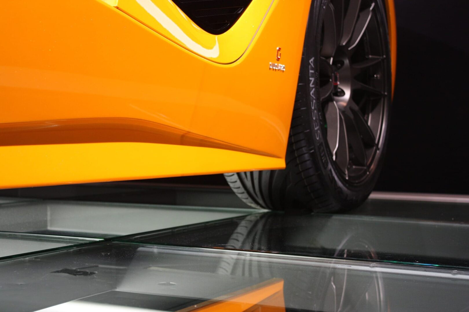 Widok z dołu na boczny profil pomarańczowego samochodu sportowego, ukazujący jego opony i szczegóły konstrukcyjne.