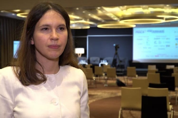 Młoda kobieta w białym żakiecie przemawiająca na konferencji.