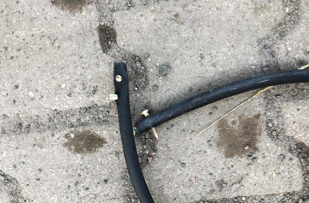 Złamany czarny wąż ze śrubami na asfalcie