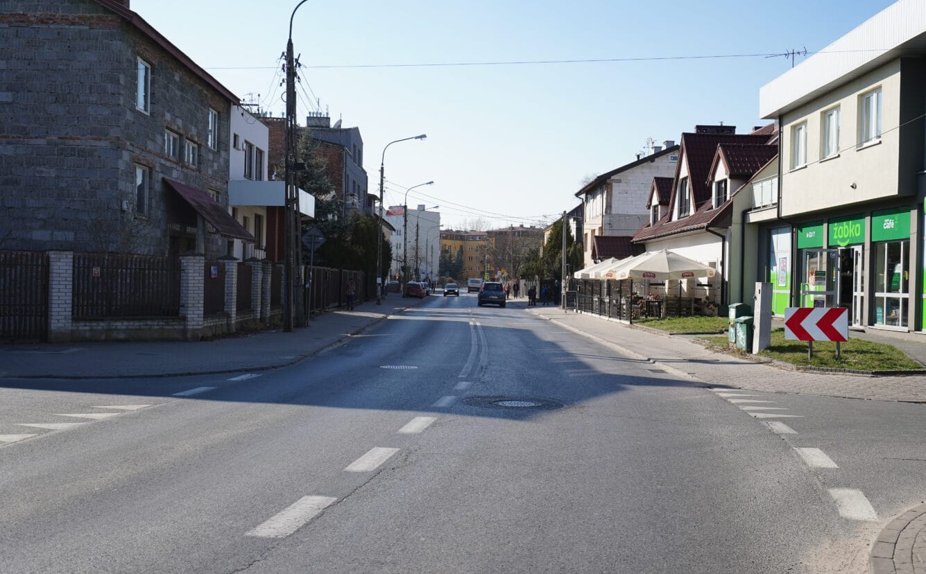 Spokojna ulica mieszkalna w Polsce, z tradycyjną zabudową i kilkoma samochodami.