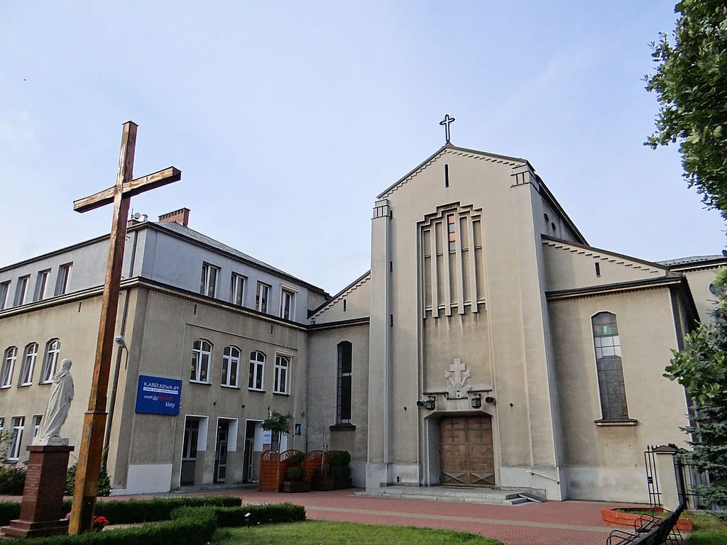 Widok zewnętrzny budynku kościoła z dużym drewnianym krzyżem i statuą.