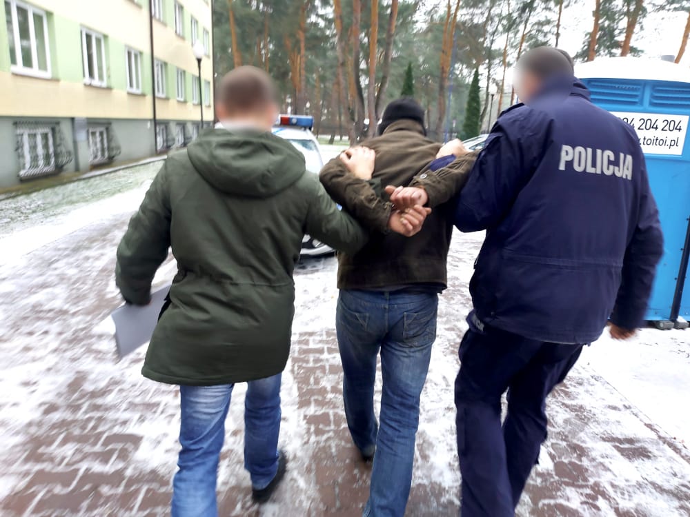 Policjanci zatrzymują podejrzanego w kajdankach na zaśnieżonej ulicy. POLICJA