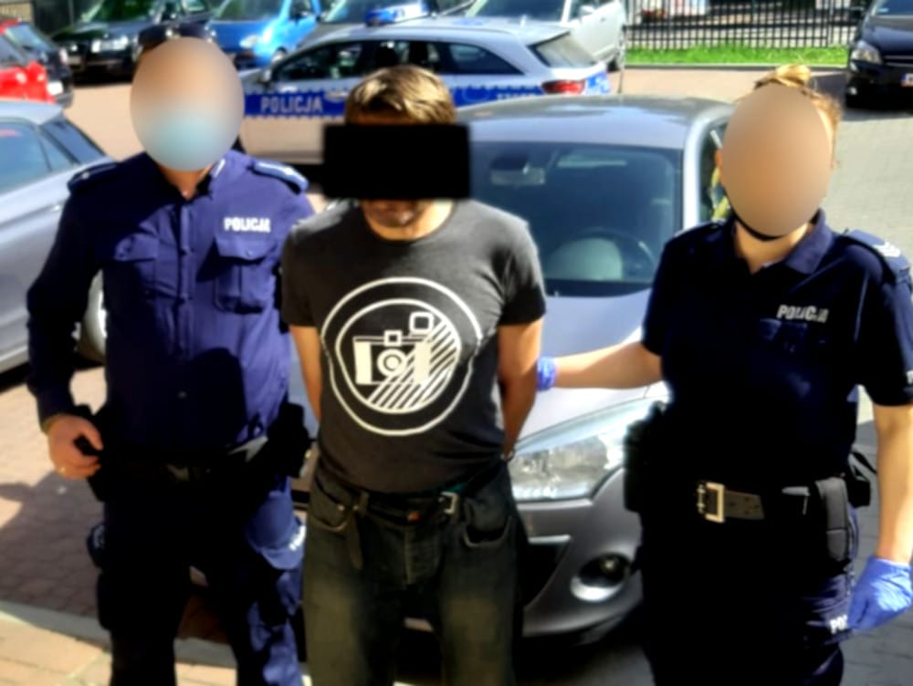 Policjanci aresztują podejrzanego w kajdankach. Na mundurach funkcjonariuszy widać napis „POLICJA”.