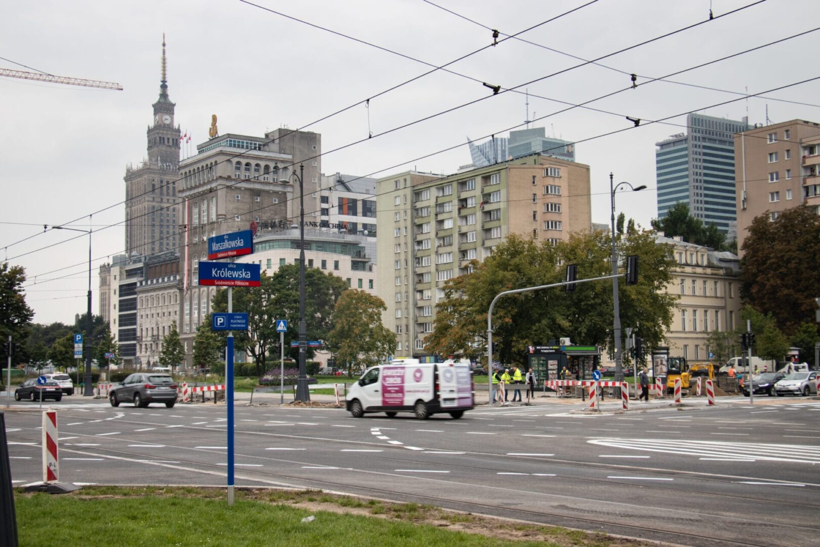 Scena uliczna Warszawy z Pałacem Kultury i Nauki w tle. Widoczny znak ul. Królewska.