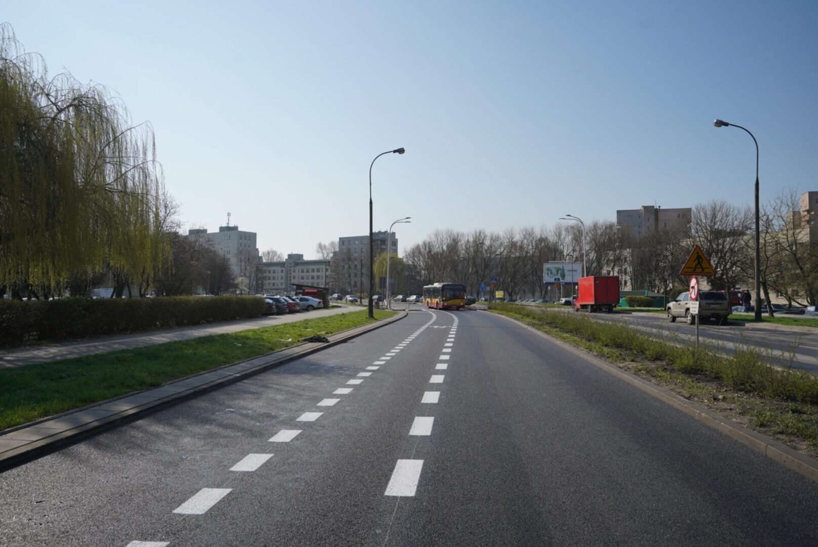 Pusta ulica miejska z oznakowaniami ścieżek rowerowych, budynkami i autobusem.