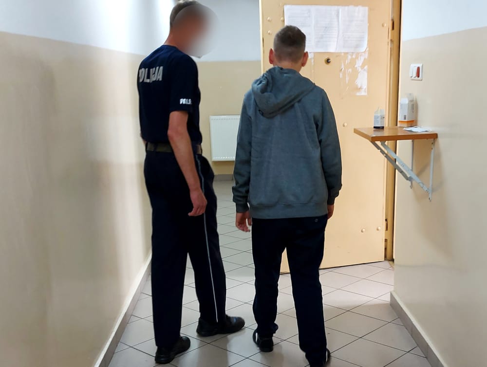 Policjant eskortujący nieletniego korytarzem.
