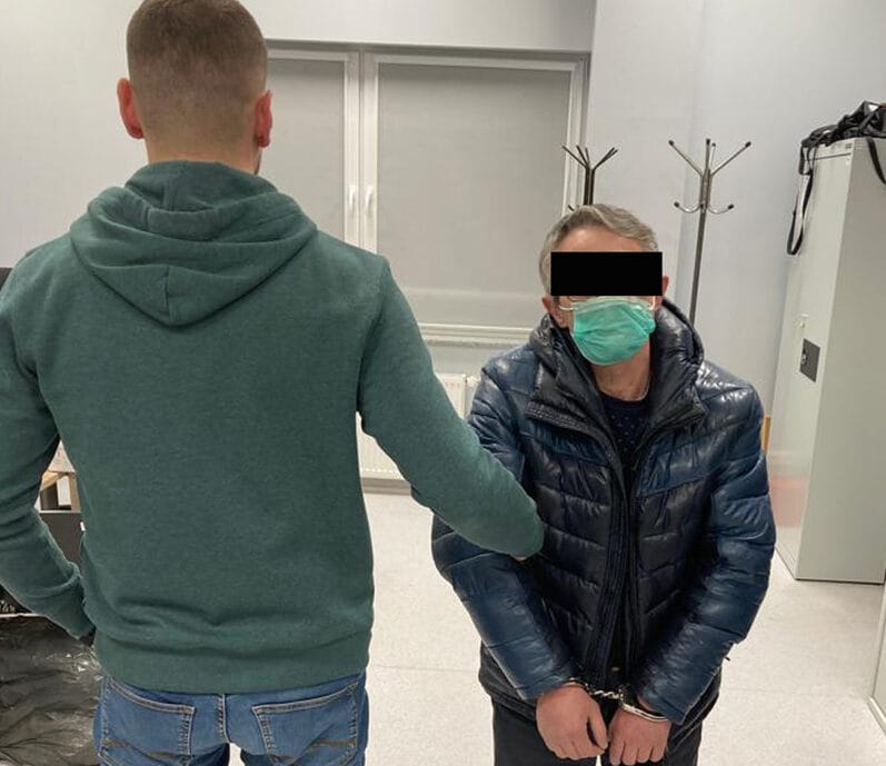 Policjant aresztujący mężczyznę w kajdankach.