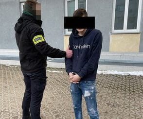 Policjant aresztujący młodego mężczyznę w kajdankach.