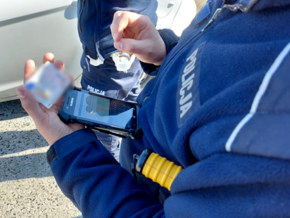 Polski policjant sprawdza prawo jazdy za pomocą urządzenia mobilnego.