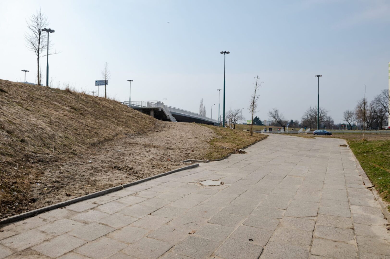 Pusta, wybrukowana ścieżka prowadząca do nowoczesnej kładki dla pieszych w pogodny dzień.