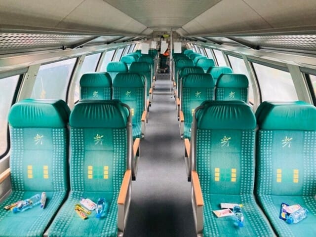 Puste, turkusowe siedzenia w pociągu skierowane do przodu, gotowe na przyjęcie pasażerów.