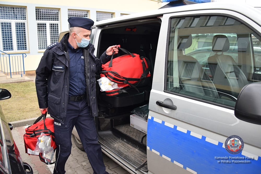 Policjant ładujący środki medyczne do radiowozu.