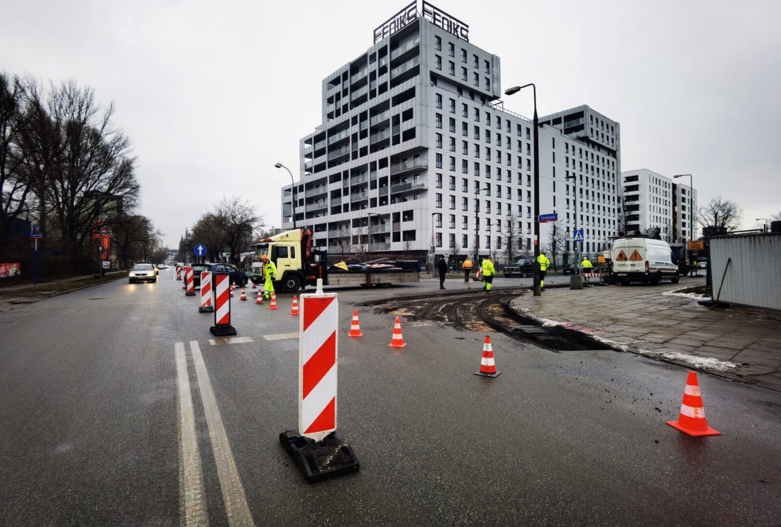 Ekipa budowlana pracująca przy budowie drogi w pobliżu nowoczesnego budynku mieszkalnego.