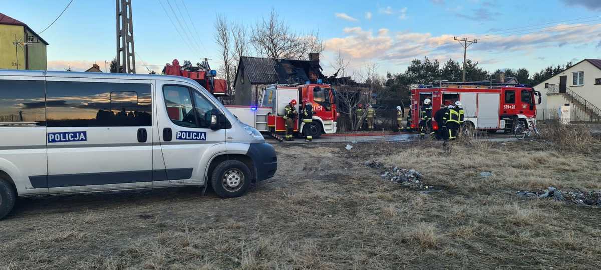 Strażacy gaszą pożar domu, policja na miejscu.
