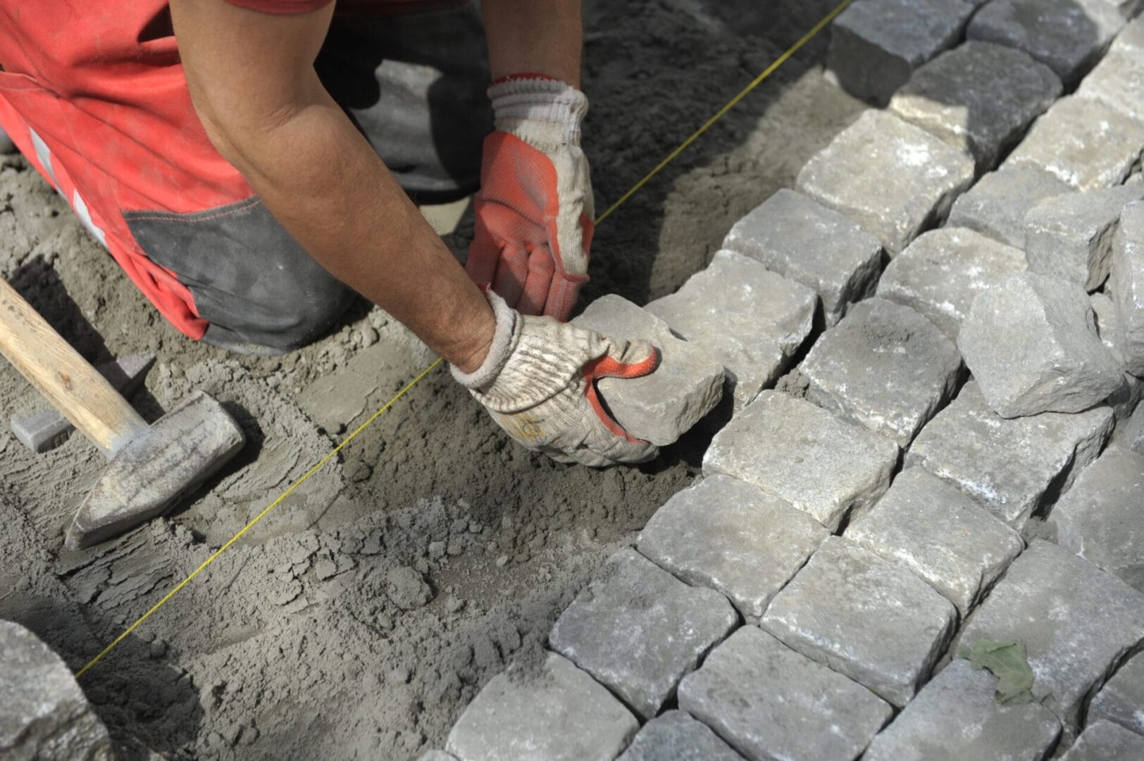 Pracownik układający kostkę brukową przy użyciu młotka i rękawiczek