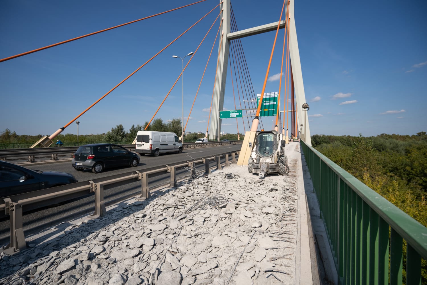 Prace drogowe na moście wantowym; mała koparka rozbija beton.